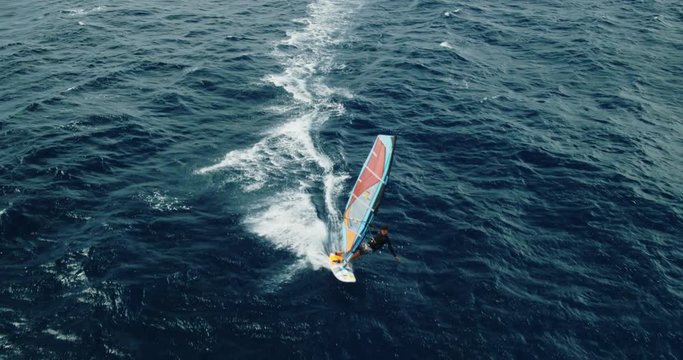 Cinematic aerial view of windsurfer sailing across the ocean from above