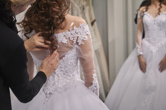 Designer assisting bride in trying wedding dress at store