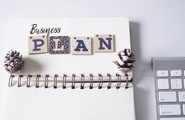 Notebook,spectacle,pinecones and computer keyboard with text BUSINESS PLAN view from top.