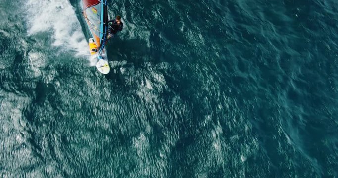 Cinematic aerial view of windsurfer sailing across the ocean from above