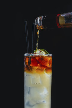 Close up of drink being poured in glass against black background