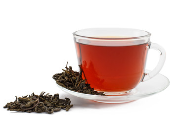 Glass cup of tea on saucer with dry leaves of green tea on white isolated background