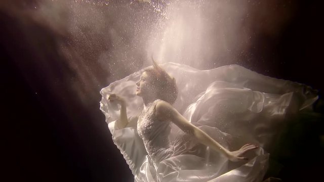 underwater magic nymph is swimming in darkness, her white big dress is floating around, she is in cloud