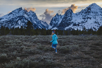 Rear view of woman running on field against mountains during winter