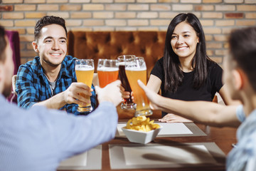 People, leisure, friendship and celebration concept - happy friends drinking craft beer and clinking glasses at bar or pub.