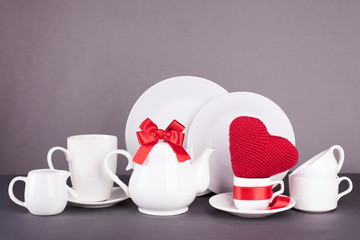 set of white dishes for lunch and tea with decor elements from red hearts and satin ribbons on a...
