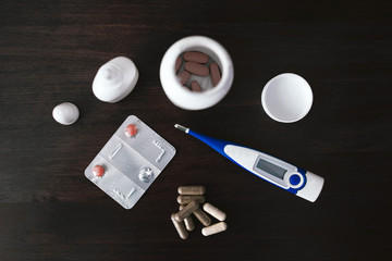 Electronic thermometer and tablets lie on a wooden table. View from above.