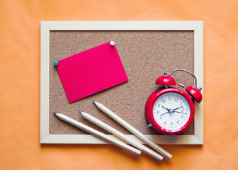 Red alarm clock, pencils and wooden board with space for the text on a orange surface. View from above
