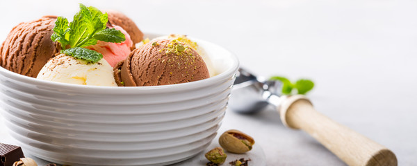 Set of ice cream scoops of different colors and flavours in white bowl with pistachio nuts and mint...
