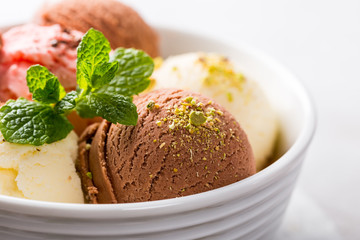 Assorted ice cream scoops of different colors and flavours in white bowl with pistachio nuts, chocolate and mint decoration. Summer food concept with copy space.