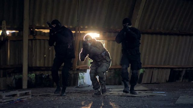 Three SWAT members walk forward with pointed rifles. 