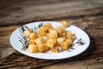 fried potato cubes with rosemary on wooden background