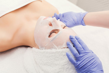 Fototapeta na wymiar Woman gets face mask by beautician at spa