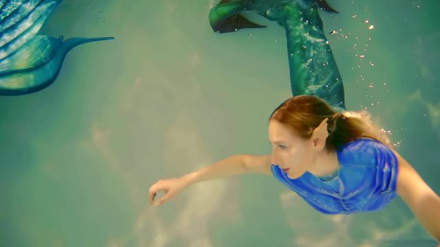 woman is dressed in mermaids costume and having fake plastic elf ears is swimming in a water