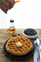 Homemade Belgian waffles with blueberries and maple syrup. A hand on a photo