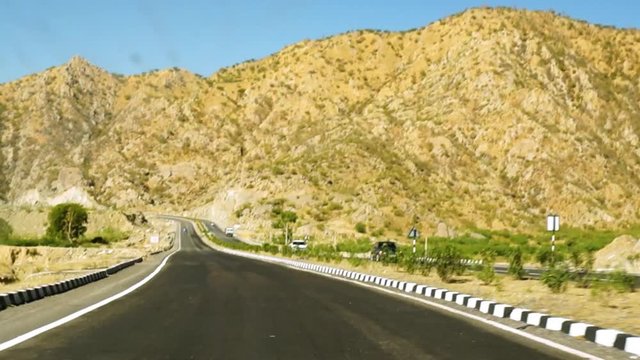 empty winding road with rocky hills towering over it shot from a moving car. Indian highways like this are very common between the cities of Rajasthan. High speed transport makes it easy to visit