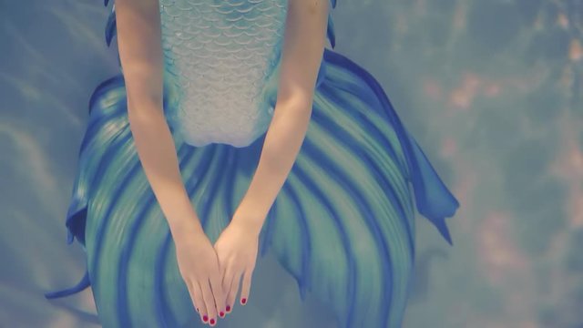 girl with blue fishtail is swimming in a pool, top view of her face, red hair, hands and plume
