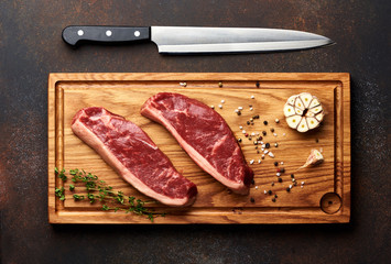 Raw fresh meat Picanha steak, traditional Brazilian cut with rosemary, garlic, knife and black pepper on wooden board. Sliced meat steaks. Top view.