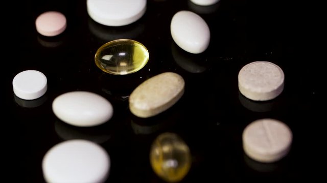 A lot of tablets on the black background. colorful pills and needle on black background, Low contrast, low key. White round tablet with two pills in background. Black background with reflection