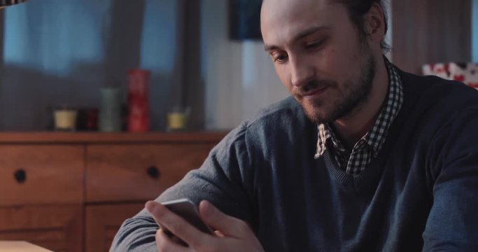Handsome young man in a stylish look using his smartphone, smiling to the phone screen. Modern communication, surfing the Internet. Having fun.