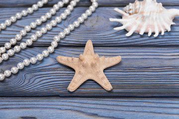 Fototapeta na wymiar a starfish, a shell, beads from pearls on a background of a blue wooden table. seafood. Marine theme