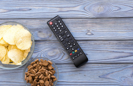 chips, crackers, a remote from the TV set on the background of a wooden table. watching television. fan.
