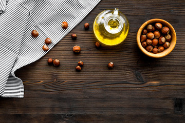 Oil as cosmetics. Haselnut oil near nut in shell on dark wooden background top view copy space