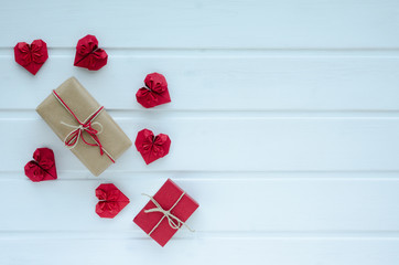 Red paper hearts with gift boxes, on white wooden background, Valentine's Day. Space to copy. Top view.