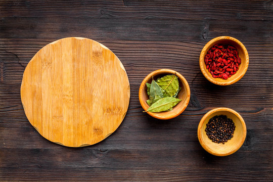 Make menu or write recipe. Mock up for menu or recipe. Wooden cutting board near ingredients in bowls bay leaf, black repper and godji on dark wooden background top view