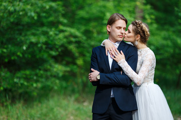 Young beautiful groom in dark blue suit and bride in white crop top dress. Happy couple on spring wedding walk