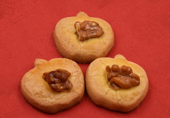 Three apple shape cookies or biscuits with one walnut on red background.