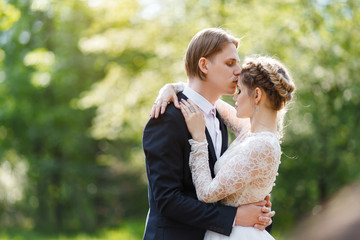 Young beautiful groom in dark blue suit and bride in white crop top dress. Happy couple on spring wedding walk