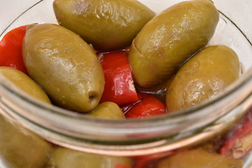 Traditional Italian spicy big green olives on a glass with oil and red peppers.