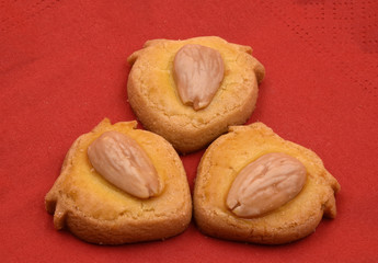 Three cookies or biscuits with almond on red background.