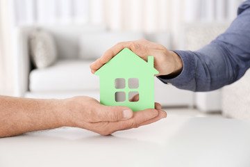 Real estate agent and senior man holding house model indoors