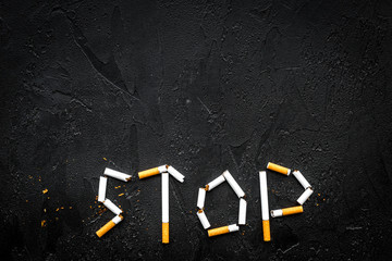 Stop smoking. Word stop lined cigarettes on black background top view copy space