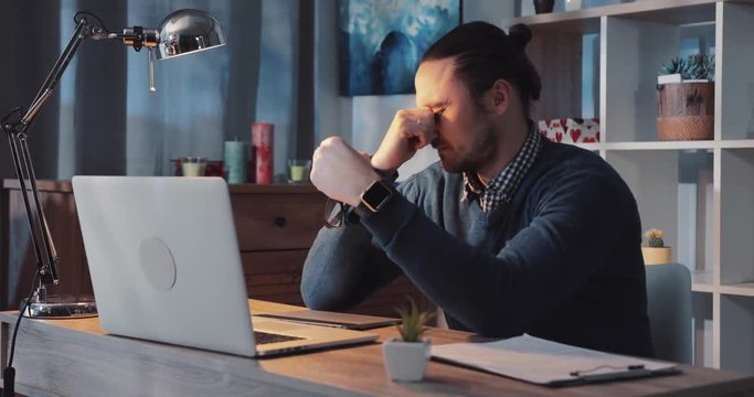 Handsome caucasian businessman works hard on the computer late at night, gets sleepy takes off the glasses, massages his nose bridge decides to have a break. Favorite job, career, successful lifestyle