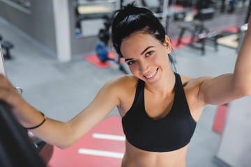 Portrait of beautiful Caucasian smile brunette woman is doing exercises with the bar in the gym, sporty woman exercising with barbell in gym, bodybuilding, people and sport concept.