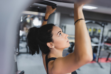 Fototapeta na wymiar Side view of beautiful Caucasian smile brunette woman is doing exercises with the bar in the gym, sporty woman exercising with barbell in gym, bodybuilding, people and sport concept.