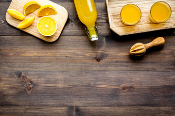 Healthy vitamin drink. Fresh orange juice near fruits and juicer on dark wooden background top view...
