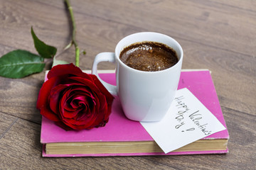coffee cup with red rose and happy valentines message card on a book