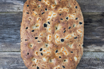 Traditional Italian focaccia homemade bread with tomatoes and black olives, on a wooden background close-up.