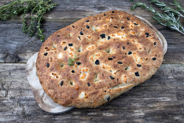 Traditional Italian focaccia homemade bread with tomatoes and olives, thyme and rosemary on a close-up wooden background.