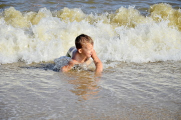 Adorable little blond kid boy having fun on ocean beach. Excited child playing with waves, swimming, splashing and happy about family vacations in Miami, Florida, USA.