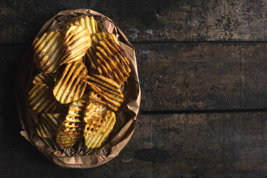 Homemade and baked potatoes chips on the wooden background with blank space