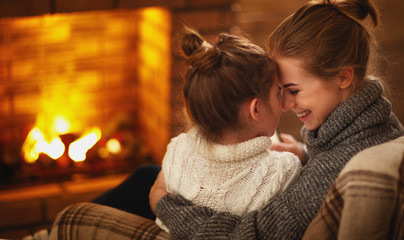 family mother and child hugs and laughing on winter evening by fireplace