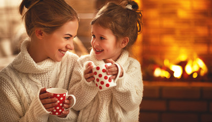 family mother and child drinking tea and laughing on winter evening by fireplace.