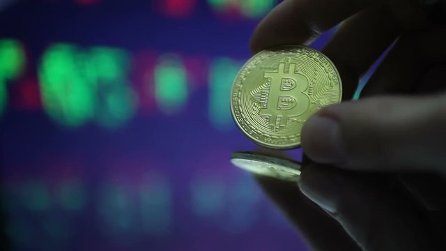 Man holds bitcoin against monitor with chart background