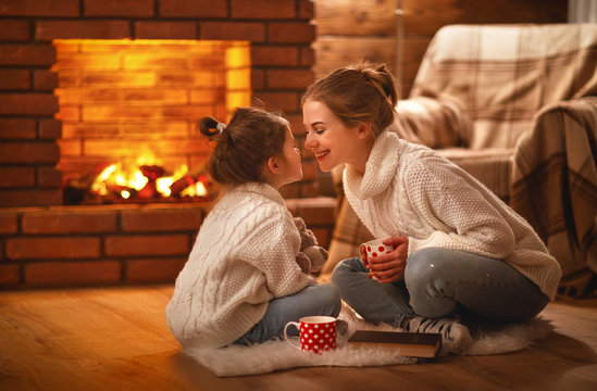 family mother and child drinking tea and laughing on winter evening by fireplace.