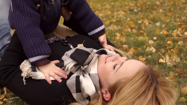 Close-up of a happy mother and son lying on the ground in an autumn park and kissing. Mom kisses her little son lying on yellow leaves in the park. 4K